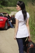 Woman with bag in foreground, man and red sports car in the background - Asia Images Group