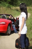 Woman standing on side of road, carrying bag, looking at man in red sports car - Asia Images Group