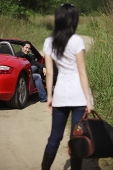 Woman standing on side of road, looking at man in red sports car - Asia Images Group