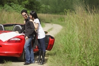 Couple standing next to red sports car, map on the car - Asia Images Group