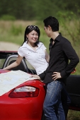 Woman leaning on red sports car, man holding map, looking at her - Asia Images Group