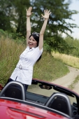 Woman standing in red sports car with arms raised - Asia Images Group