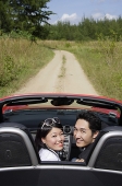 Couple in convertible car, turning to look at camera - Asia Images Group