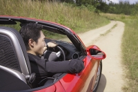 Man driving red convertible sports car along country road - Asia Images Group