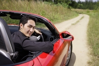 Man driving red convertible sports car, turning to look at camera - Asia Images Group