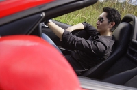 Man wearing sunglasses, driving red convertible sports car - Asia Images Group