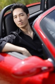 Man sitting in red convertible car, portrait - Asia Images Group