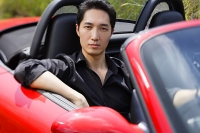 Man sitting in red convertible car, looking at camera, portrait - Asia Images Group