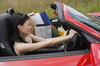 Woman driving convertible car, shopping bags next to her - Asia Images Group