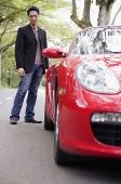 Man standing and looking at rear of red sports car - Asia Images Group