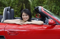 Woman sitting in red sports car, smiling at camera, portrait - Asia Images Group