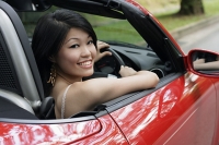 Woman driving red sports car, turning to smile at camera - Asia Images Group