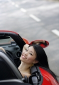 Woman sitting in red sports car, leaning head on door, smiling at camera - Asia Images Group