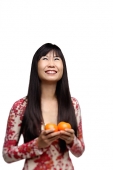 Woman with long straight hair, holding two oranges, looking up - Asia Images Group
