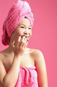 Woman wrapped in a pink towel, hand over mouth - Asia Images Group