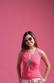 Woman dressed in pink, wearing sunglasses, standing against pink background, - Asia Images Group