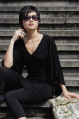 Woman dressed in black, wearing large sunglasses, sitting on steps - Asia Images Group