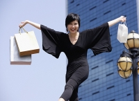 Woman dressed in black, arms outstretched, carrying shopping bags - Asia Images Group