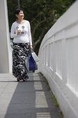 Mature woman carrying shopping bags, walking along bridge - Asia Images Group