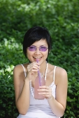 Woman drinking from a straw, smiling at camera - Asia Images Group