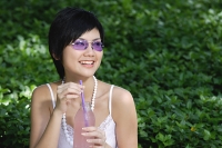 Woman in purple sunglasses, holding drink, looking away - Asia Images Group