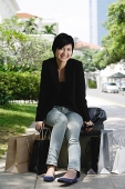 Woman sitting in city, shopping bags around her, smiling at camera - Asia Images Group