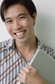 Man smiling at camera, holding laptop - Asia Images Group