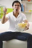 Man holding bowl of popcorn, making a fist - Asia Images Group