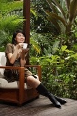 Woman sitting on patio, having cup of tea - Asia Images Group