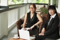 Two businesswomen sitting on patio with laptop, looking at camera - Asia Images Group
