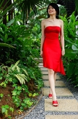 Woman wearing red dress, walking along garden path - Asia Images Group