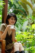 Woman sitting on patio, holding cup and saucer - Asia Images Group
