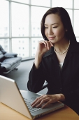 Portrait of businesswoman using laptop, hand on chin - Asia Images Group