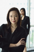 Businesswoman looking at camera, arms crossed, another woman in the background - Asia Images Group