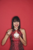 Woman dressed in red cheongsam, eating bowl of rice - Asia Images Group
