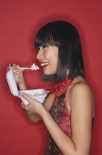 Woman standing red background, eating rice from a Styrofoam container - Asia Images Group