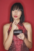 Woman dressed in cheongsam, holding mobile phone, finger on chin - Asia Images Group