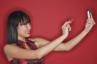 Woman standing against red background, using PDA - Asia Images Group