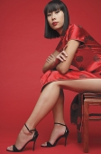 Woman wearing cheongsam and high heels, sitting on chair - Asia Images Group