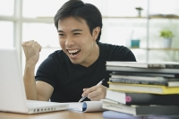Young adult looking at laptop, smiling, making a fist - Asia Images Group