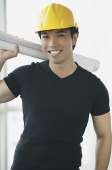 Young adult wearing hardhat, carrying blueprints over his shoulder - Asia Images Group