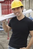 Young man wearing hardhat, carrying blueprints - Asia Images Group