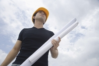Young man wearing hardhat, carrying blueprints, low angle view - Asia Images Group