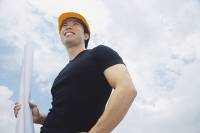 Young man in hardhat, carrying blueprints, smiling - Asia Images Group