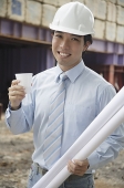 Businessman wearing hardhat, carrying blueprints and a cup - Asia Images Group