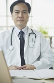 Doctor sitting at desk, looking at camera, serious expression - Asia Images Group