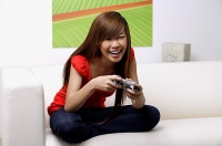 Young woman sitting on sofa, holding TV remote control - Asia Images Group