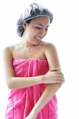 Young woman wearing shower cap and towel, applying moisturizer to arm - Asia Images Group