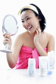 Young woman sitting at dressing table, looking in mirror, hand on chin - Asia Images Group