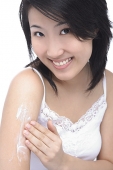 Young woman applying moisturizer on arm, smiling at camera - Asia Images Group